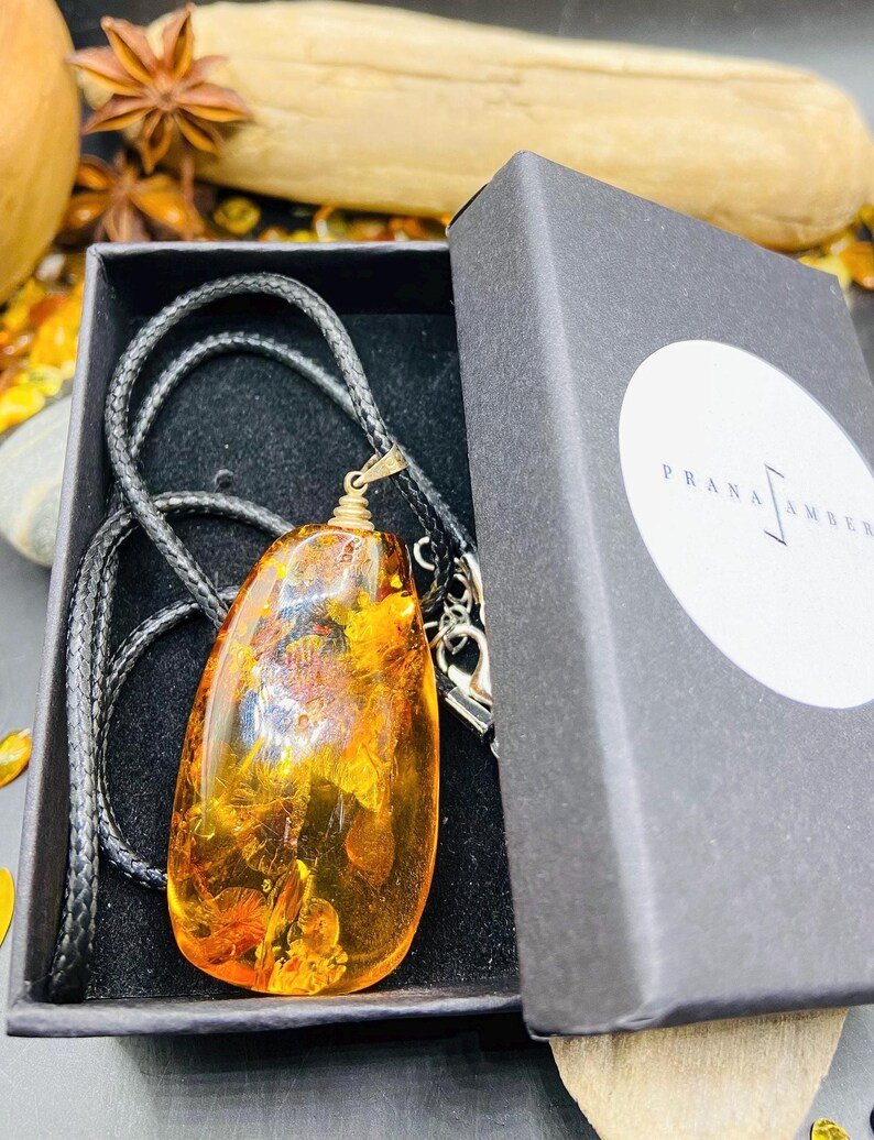 Oranžas krāsas pulēts Baltijas Dzintara kulons ar melnu aukliņu