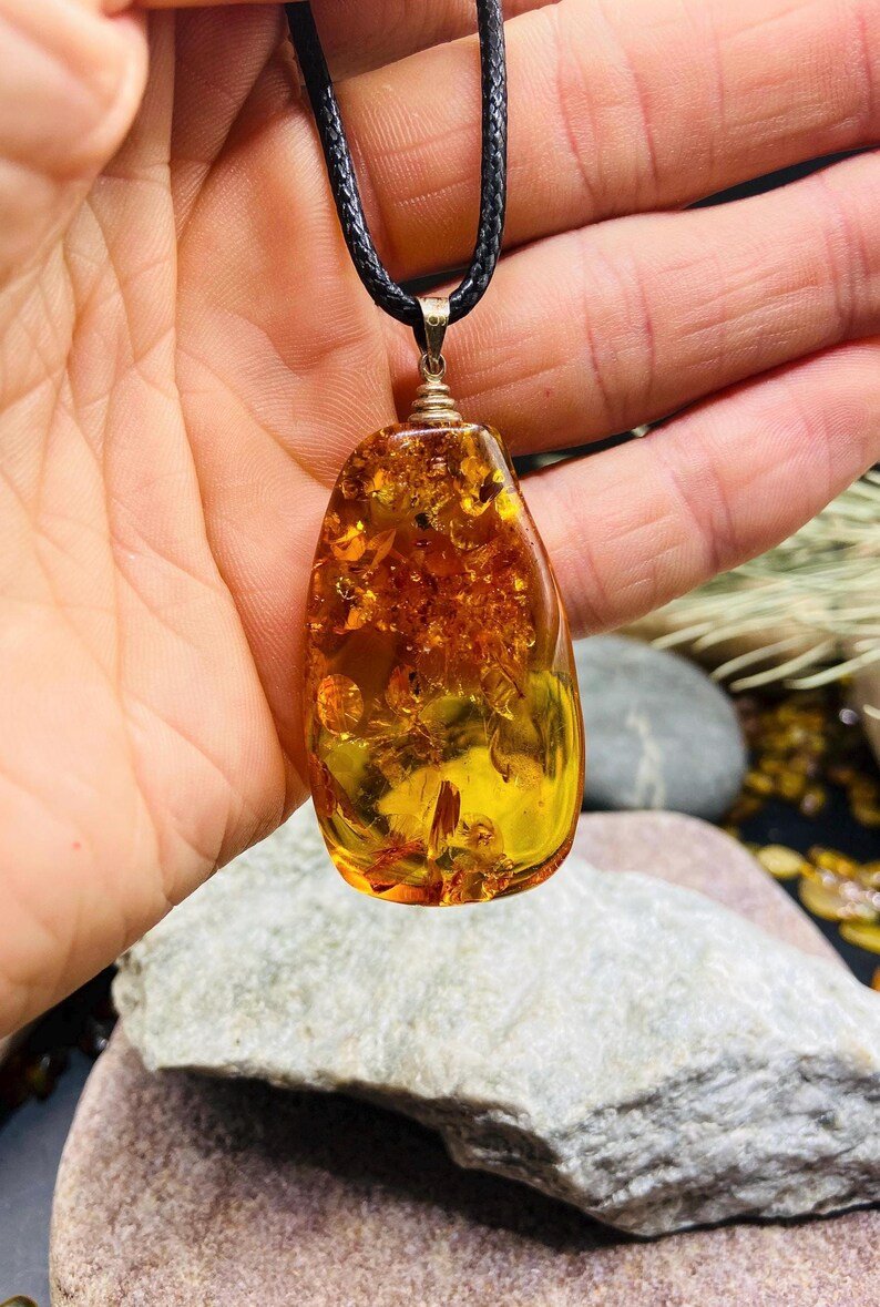 Oranžas krāsas pulēts Baltijas Dzintara kulons ar melnu aukliņu