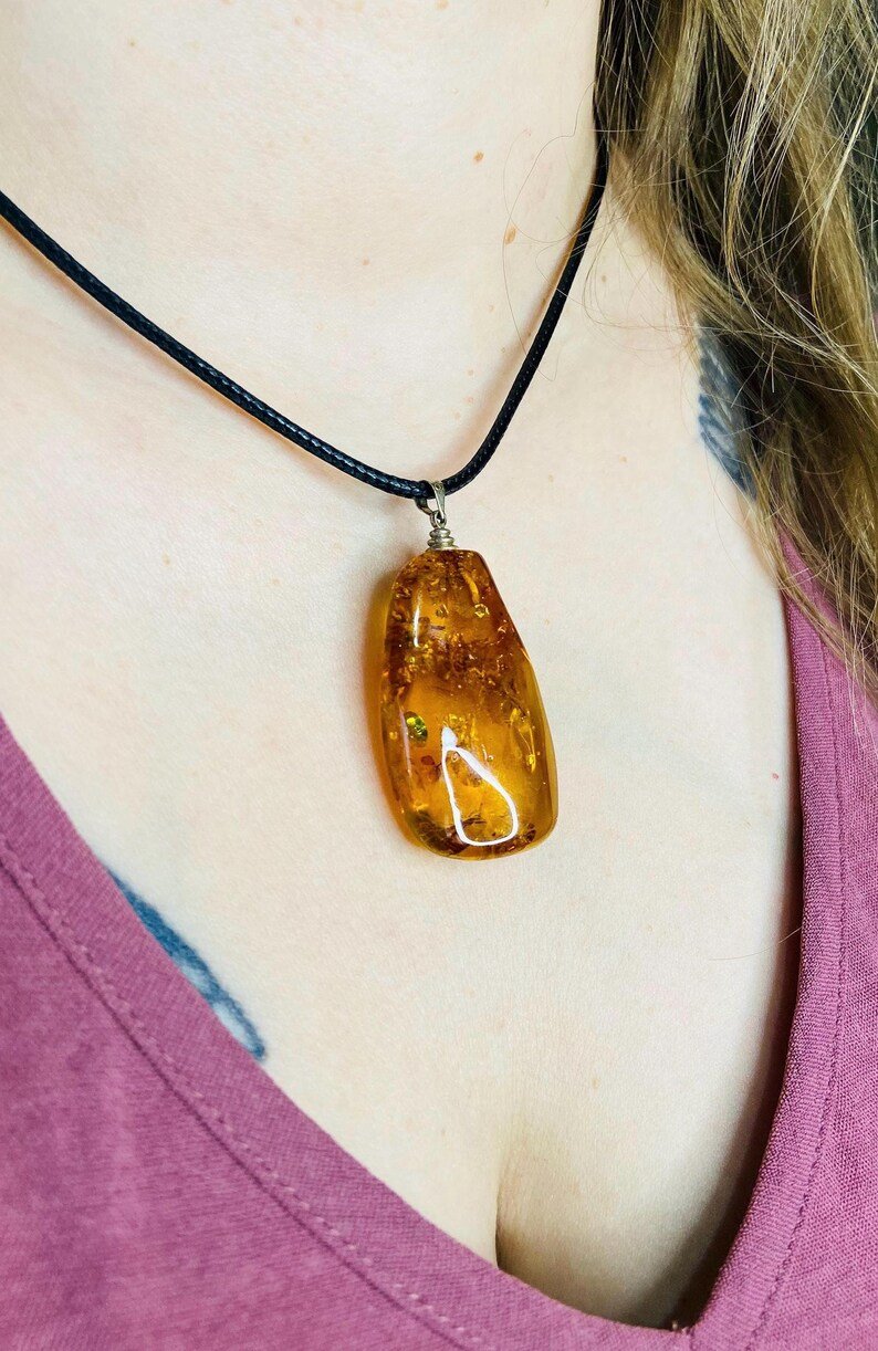 Oranžas krāsas pulēts Baltijas Dzintara kulons ar melnu aukliņu