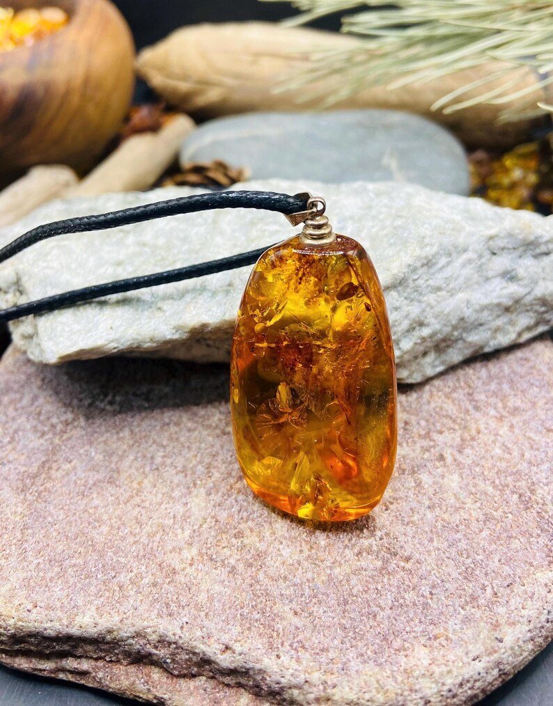 Oranžas krāsas pulēts Baltijas Dzintara kulons ar melnu aukliņu
