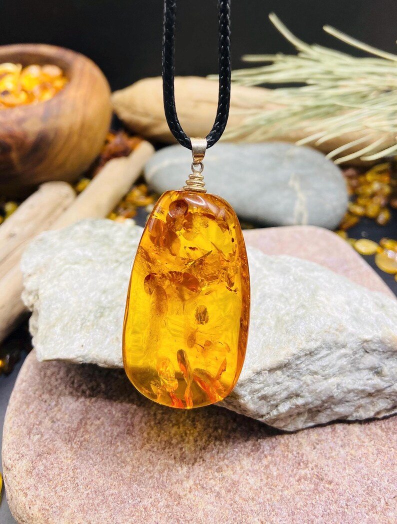 Oranžas krāsas pulēts Baltijas Dzintara kulons ar melnu aukliņu