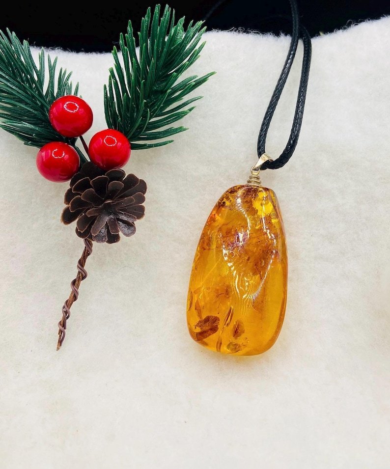 Oranžas krāsas pulēts Baltijas Dzintara kulons ar melnu aukliņu