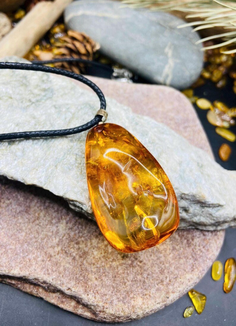 Oranžas krāsas pulēts Baltijas Dzintara kulons ar melnu aukliņu